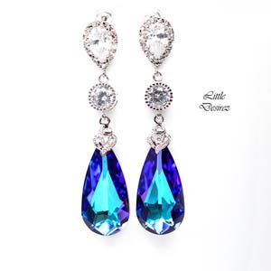 May include: A pair of silver dangle earrings with teardrop-shaped blue and teal crystals. The earrings have a small round crystal above the teardrop crystal and a larger oval crystal at the top.