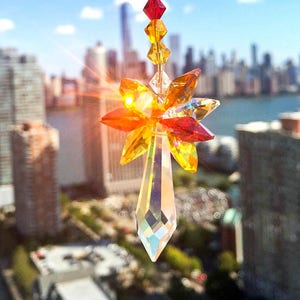 May include: A crystal suncatcher with a clear teardrop-shaped prism and a starburst of orange, yellow, and red crystals. The suncatcher is hanging from a chain of clear, orange, and red crystals.