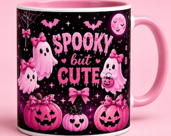 May include: A ceramic mug with a pink interior and handle, featuring a black background decorated with pink ghosts, pumpkins, bats, and bows. The text SPOOKY but CUTE is printed in pink, dripping-style lettering across the center of the mug.
