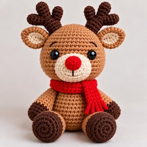 Puede incluir: Un peluche de reno tejido a ganchillo con cuerpo marrón claro, astas marrón oscuro y pies marrón oscuro. El reno tiene un hocico color crema, una nariz roja brillante, ojos de plástico negro y lleva una bufanda roja tejida.