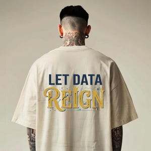 Pode incluir: Uma t-shirt bege de manga curta com o texto LET DATA REIGN impresso nas costas. As palavras LET DATA estão em azul escuro, enquanto REIGN está numa fonte dourada grande com um pequeno ícone de coroa e gráficos subtis.
