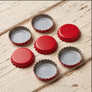 May include: A collection of six circular metal bottle caps with a bright red exterior finish. Three caps are positioned with the smooth red top facing upward, while three caps are flipped to reveal the light gray interior with the number 16.