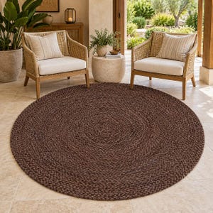 Può includere: Un grande tappeto circolare caratterizzato da una trama intrecciata color marrone scuro. Il tappeto è realizzato in fibre naturali intrecciate, creando un motivo concentrico denso e uniforme che si irradia dal centro verso il bordo esterno.
