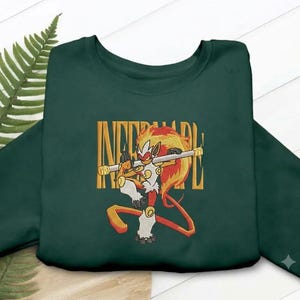 Könnte beinhalten: Ein dunkelgrüner Rundhals-Pullover mit einer Stickerei eines feuerartigen Affenwesens, das einen Stab hält. Die Kreatur hat rotes, oranges und weißes Fell mit Flammen auf dem Kopf. Der Text INFERNAPE ist in Gelb im Hintergrund aufgestickt.