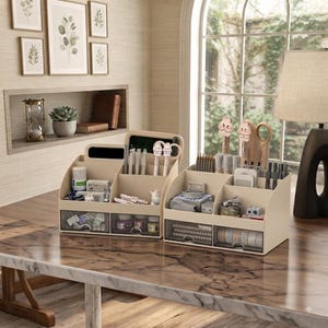May include: Two beige plastic desk organisers with multiple compartments and two clear drawers each. The organisers hold various stationery items including pens, pencils, tape, clips, and small bottles, featuring decorative character-topped pens.