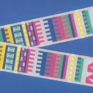 May include: White ribbon with a colorful geometric pattern. The pattern includes pink, blue, green, yellow, and white stripes and shapes.