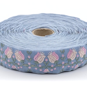 Pode incluir: Rolo de fita azul claro com um desenho floral bordado. A fita apresenta flores rosa e creme com folhas e caules verdes. Adequado para artesanato ou projetos de costura.