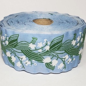 Cinta jacquard KAFKA H-02/03 de algodón orgánico tejido, 38 mm de ancho, fondo azul claro, lirios del valle blancos y hojas/tallos verdes.