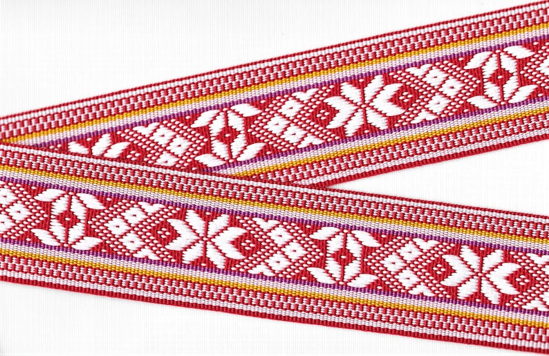 May include: Red, white, purple, and gold woven ribbon with a geometric pattern. The ribbon is made of a soft, textured fabric.