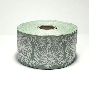 Op de afbeelding: Een rol groene bies met een wit bloemenpatroon. De bies is gemaakt van een zachte, geweven stof en heeft een subtiele glans.