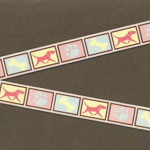 May include: A white ribbon with a repeating pattern of pink paw prints, yellow bones, and red dogs. The ribbon is on a brown background.