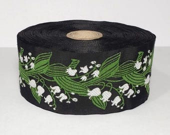 May include: Black ribbon with a white and green floral pattern. The pattern features lily of the valley flowers and leaves.