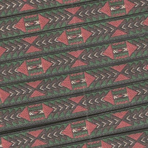 May include: Close-up of a woven fabric with a repeating geometric pattern in shades of green, red, and brown. The pattern features triangles, arrows, and squares.