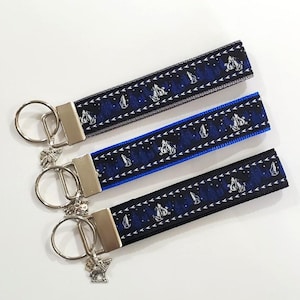 May include: Three keychains with matching patterned wrist straps. The straps feature a dark blue background with white mountain and star designs. Each keychain has a silver-colored metal clasp and a decorative charm.