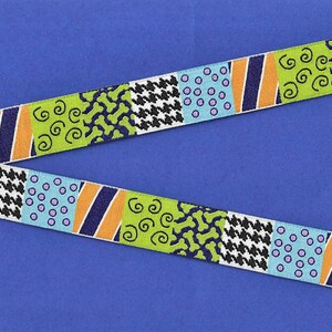 May include: A colorful ribbon with a repeating pattern of green, blue, orange, black, and white. The pattern includes swirls, polka dots, and houndstooth.