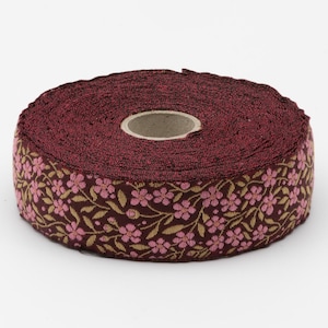 May include: A roll of fabric ribbon featuring a deep burgundy background with a repeating pattern of small pink flowers and light gold leaves. The ribbon is wound around a central cardboard core, displaying a textured, woven appearance.