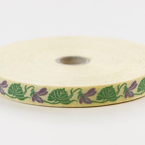 Cinta jacquard KAFKA C-01/03 de algodón orgánico tejido, 16 mm de ancho, fondo amarillo con violetas moradas y hojas/enredaderas verdes.