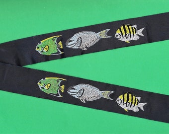 May include: Black ribbon with a repeating pattern of embroidered fish. The fish are green, yellow, and white.