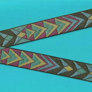 Puede incluir: Dos tiras de cinta estampada con un diseño geométrico. La cinta presenta un fondo verde oliva oscuro con formas de flecha repetidas en turquesa, magenta, amarillo y azul claro. La cinta está sobre un fondo turquesa.