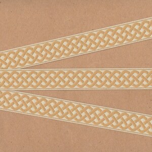 May include: Three beige ribbon trims with a woven Celtic knot design. The ribbon trims are on a brown background.