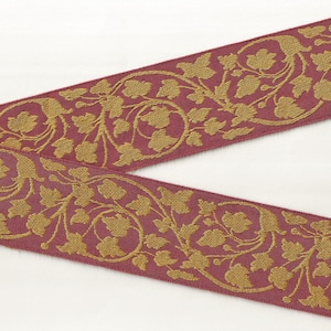 May include: Burgundy red ribbon with a gold floral pattern. The pattern features intricate leaves and vines.