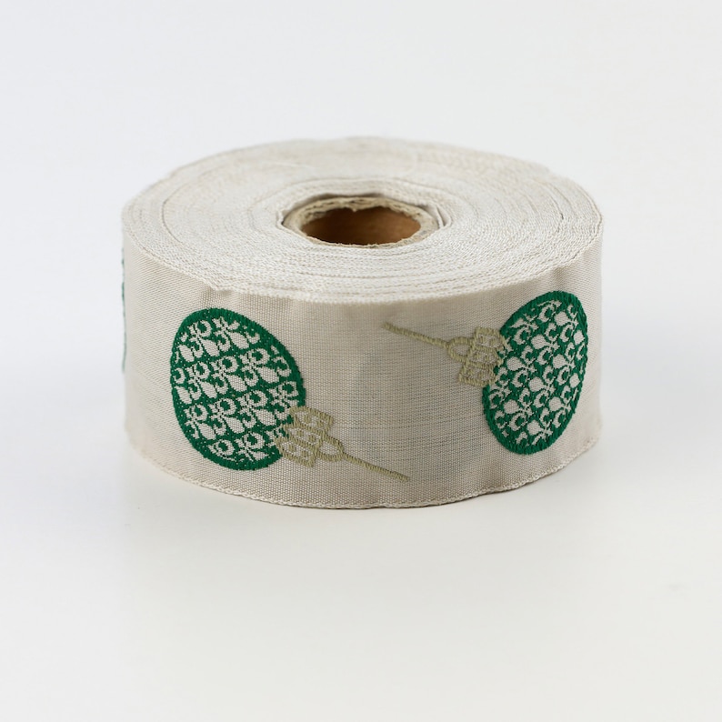 Puede incluir: Un rollo de cinta blanca con un dise&ntilde;o estampado verde y dorado. El patr&oacute;n presenta un motivo repetido de un c&iacute;rculo con un dise&ntilde;o estilizado en su interior.