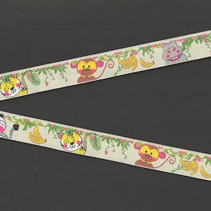 May include: A beige ribbon with a repeating pattern of jungle animals, including a zebra, tiger, monkey, and hippopotamus. The animals are surrounded by green leaves and pink flowers. There are also yellow bananas on the ribbon.