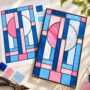 May include: A rectangular stained glass panel featuring a geometric design with two semi-circles in pink and white, surrounded by blue, light blue, and pink glass segments. A numbered pattern guide with colour codes is visible next to the panel.