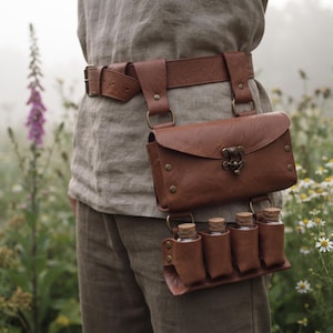 Peut inclure: Une ceinture en cuir marron dotée d'une pochette rectangulaire avec un fermoir en métal couleur laiton et quatre petits étuis en cuir contenant des flacons en verre transparent avec des bouchons en liège, fixés par des rivets en laiton.