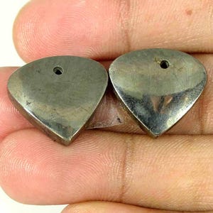 May include: Two heart-shaped pendants with a metallic, dark grey, reflective surface. Each piece features a single, small, circular hole positioned near the top centre, designed for threading or attachment in jewellery making projects.