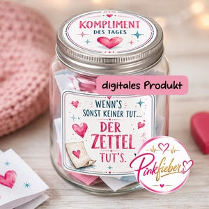 May include: A clear glass jar with a silver lid, featuring a label that reads KOMPLIMENT DES TAGES and WENN'S SONST KEINER TUT... DER ZETTEL TUT'S. The jar contains small folded papers with heart illustrations and includes a Pinkfieber logo sticker.