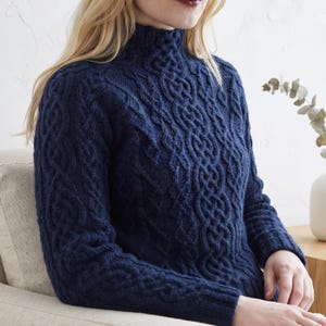 May include: A dark navy blue long-sleeve sweater featuring a high mock neck collar and an intricate, raised cable knit pattern that covers the front and sleeves. The knit design consists of repeating braided and interlocking geometric shapes.