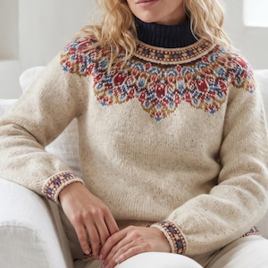 Könnte beinhalten: Ein cremefarbener Strickpullover mit dunkelblauem Rollkragen und einem dekorativen Muster an der Passe in Rot-, Blau- und Brauntönen. Das langärmelige Kleidungsstück verfügt über passende gemusterte Bündchen und eine gesprenkelte Textur.