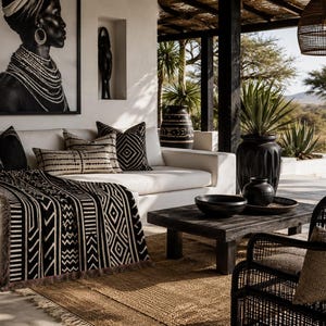 May include: A white sofa featuring black and white patterned throw pillows and a matching throw blanket with geometric designs. A black wooden coffee table sits in front, holding a black bowl and vase, near a black woven chair and rug.