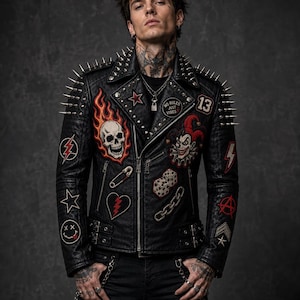 May include: A black leather motorcycle jacket featuring silver metal spikes on the shoulders and lapels. The jacket is decorated with various embroidered patches including a flaming skull, a jester, dice, a broken heart, and the text No Rules Just Vibes.