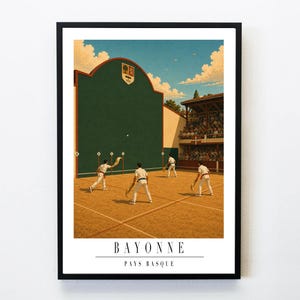 Puede incluir: Una lámina enmarcada que representa un partido de pelota vasca en una cancha de tierra con un gran frontón verde que muestra un escudo. Cuatro jugadores con uniformes blancos sostienen cestas curvas. El texto BAYONNE PAYS BASQUE aparece abajo.