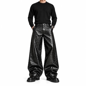 Könnte beinhalten: Ein schwarzer langärmliger Pullover mit Rundhalsausschnitt kombiniert mit einer weiten Hose mit glänzender, schwarzer Krokodilprägung. Die Hose verfügt über einen Knopfverschluss, Gürtelschlaufen und einen lockeren Schnitt, der bis zu schwarzen Stiefeln reicht.