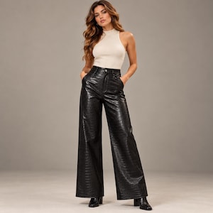 Puede incluir: Un top sin mangas de color crema con cuello alto combinado con pantalones negros de cintura alta que presentan un patrón texturizado de piel de cocodrilo. Los pantalones tienen una silueta de pierna ancha, cierre de botón y cremallera.