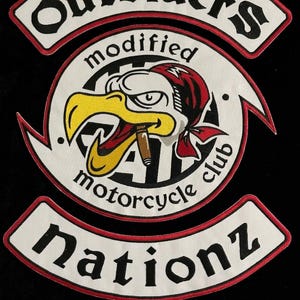 May include: A circular embroidered patch featuring a central eagle head wearing a red bandana and smoking a cigar. The text reads Outsider's modified motorcycle club Nationz. The design uses white, black, red, and yellow thread on a black background.