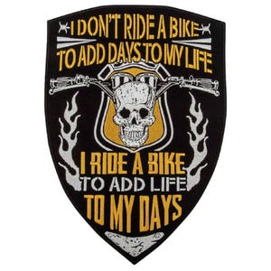 Könnte beinhalten: Ein schildförmiger, schwarzer Aufnäher mit einem weißen Totenkopf, der über einem Motorradlenker zentriert ist. Der gelbe Text lautet: I DON'T RIDE A BIKE TO ADD DAYS TO MY LIFE I RIDE A BIKE TO ADD LIFE TO MY DAYS. Weiße Flammenmuster flankieren den Totenkopf.