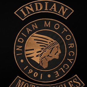 Könnte beinhalten: Ein schwarzes Stoffaufnäher-Set mit goldener Stickerei. Der obere Bogen trägt die Aufschrift INDIAN. Das zentrale kreisförmige Emblem zeigt das Profil einer Person mit Kopfschmuck, umgeben vom Text INDIAN MOTORCYCLE 1901. Der untere Bogen zeigt MOTORCYCLES.