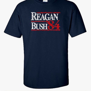 May include: A navy blue t-shirt with a white and red distressed graphic that reads "Reagan Bush '84".