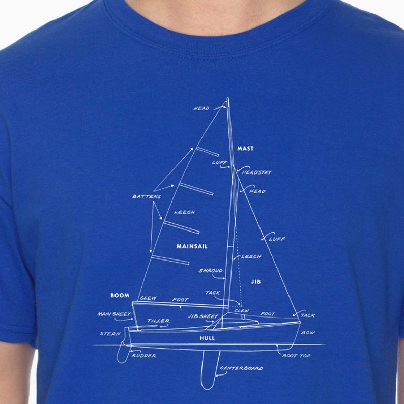 May include: A blue t-shirt with a white outline of a sailboat and its parts labeled. The labels include: head, mast, headstay, luff, leech, mainsail, shroud, jib, boom, clew, foot, tack, main sheet, jib sheet, tiller, stern, rudder, hull, bow, boot top, and centerboard.