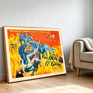 May include: A framed film poster for From Hell It Came featuring a large blue monster with yellow eyes and sharp teeth against a bright orange and yellow flame background. A person in a white dress is falling while a sword pierces the monster.