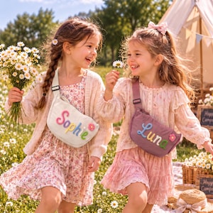 May include: Two crossbody bags with adjustable straps, one off-white and one mauve. The off-white bag features the name Sophie in colorful raised letters with a small pink flower. The mauve bag features the name Luna in colorful raised letters with a small pink flower. Both bags are worn across the chest.