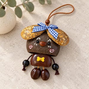 May include: A decorative hanging ornament crafted from natural materials, featuring a dark brown coconut shell head with painted white details, a blue and white gingham bow, a yellow bone-shaped charm, and dark brown seed-like limbs and feet.