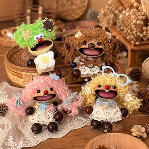 Peut inclure: Quatre poupées artisanales aux cheveux en laine bouclée verts, marron, roses et jaunes. Chaque poupée présente une large bouche ouverte, un nez rouge et une robe en dentelle blanche. Elles ont des mains et pieds en perles marron foncé et des accessoires.
