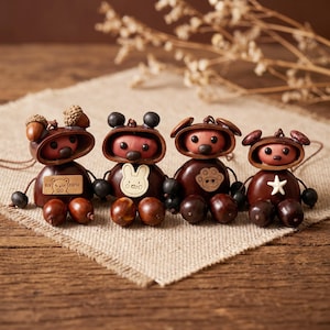 May include: Four handcrafted figurines made from brown chestnuts and acorns. Each figure has a round pink face, dark eyes, and a nose. They feature unique chest decorations: a bear, a rabbit, a paw print, and a white star. They have small limbs.