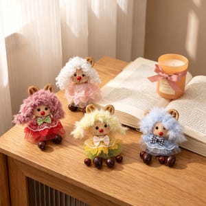 Può includere: Quattro piccole bambole decorative con capelli soffici rosa, bianchi, gialli e blu. Ogni bambola presenta un viso rotondo, un naso rosso e un vestito di pizzo a strati con un piccolo fiocco. Le bambole hanno piedi a forma di perla marrone scuro.