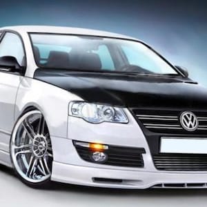 Pode incluir: Um sedã Volkswagen branco com capô preto contrastante, grade frontal preta com emblema Volkswagen, rodas cromadas de raios múltiplos e suspensão rebaixada. O para-choque dianteiro inclui luzes de neblina integradas.